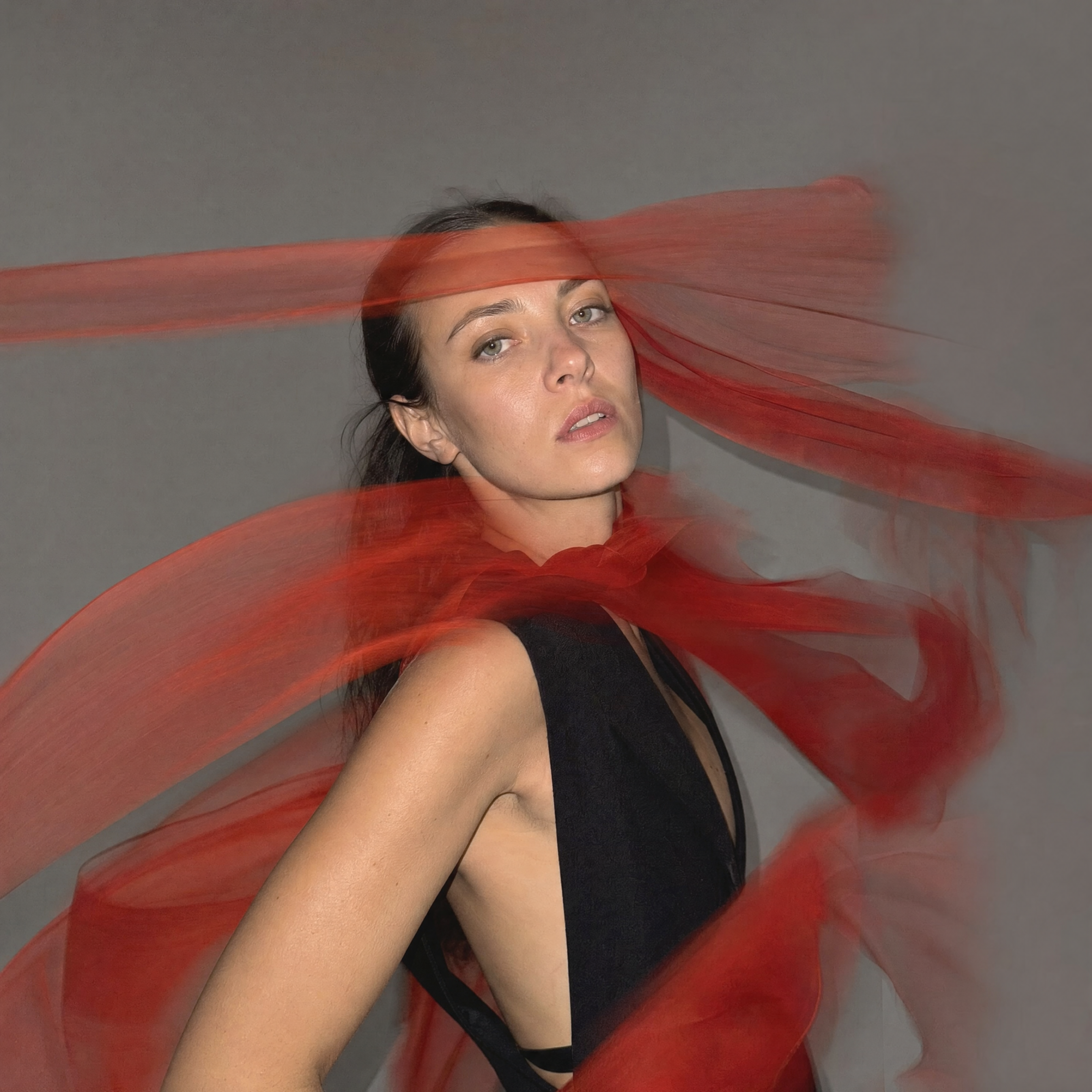 AI text-to-image result — An elegant adult model in a minimal black tailored dress while an extremely long translucent red scarf moves r…